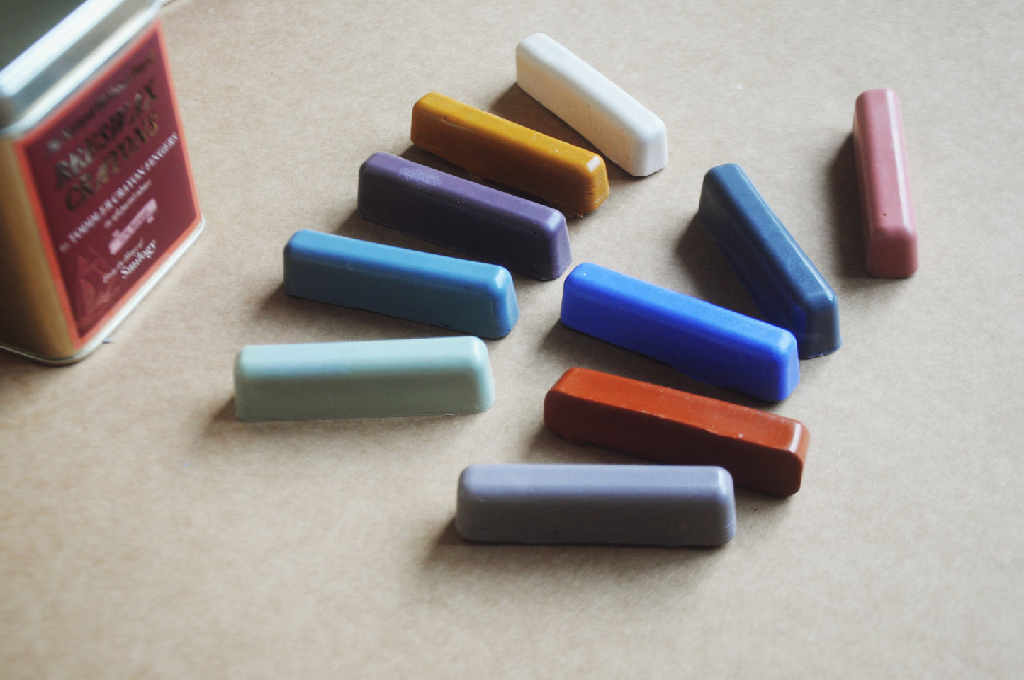 Set of colourful wax crayons in soft pastel shades with a tin container on a beige surface close up