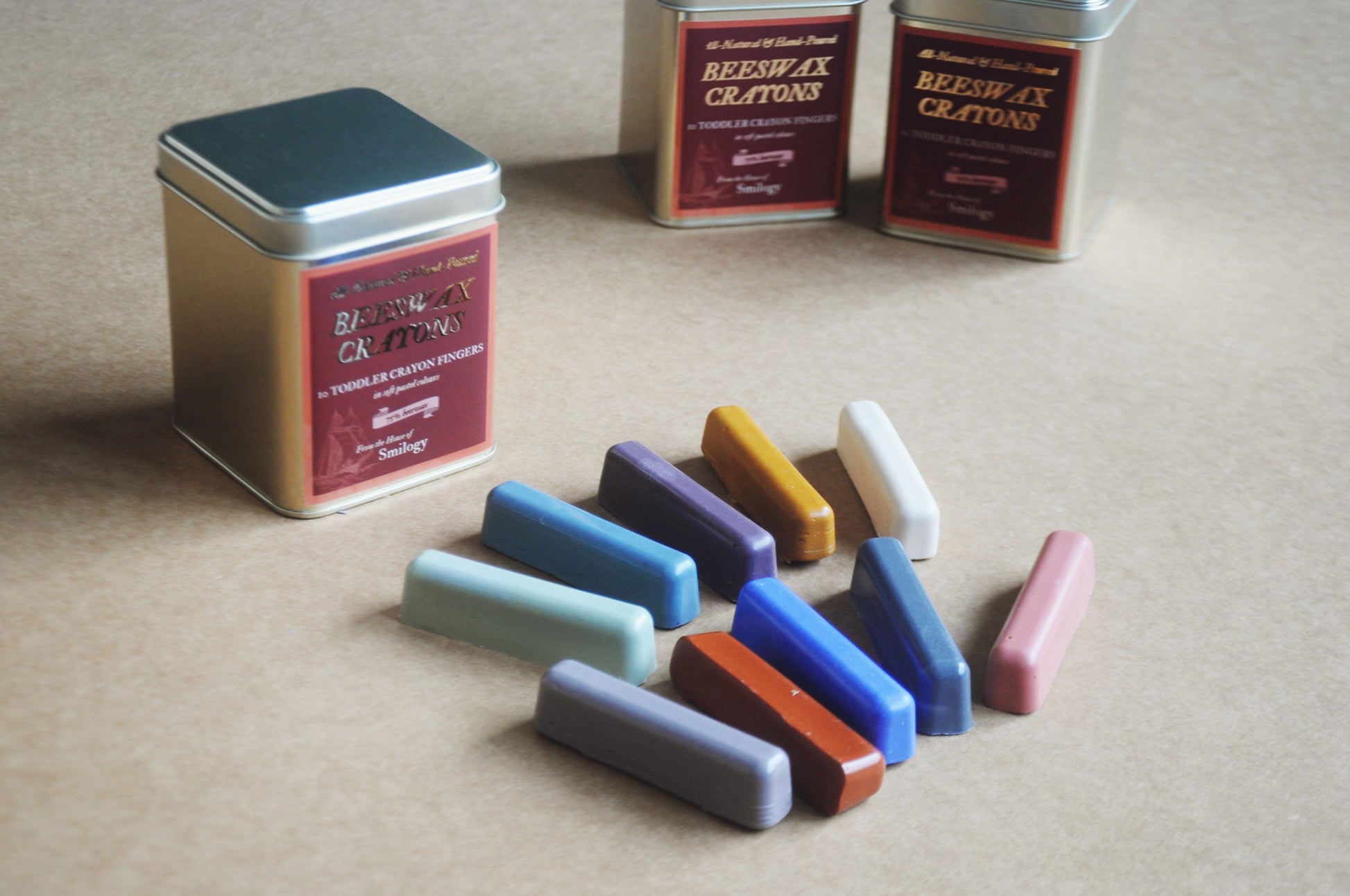 Set of colourful wax crayons in soft pastel shades with a tin container on a beige surface
