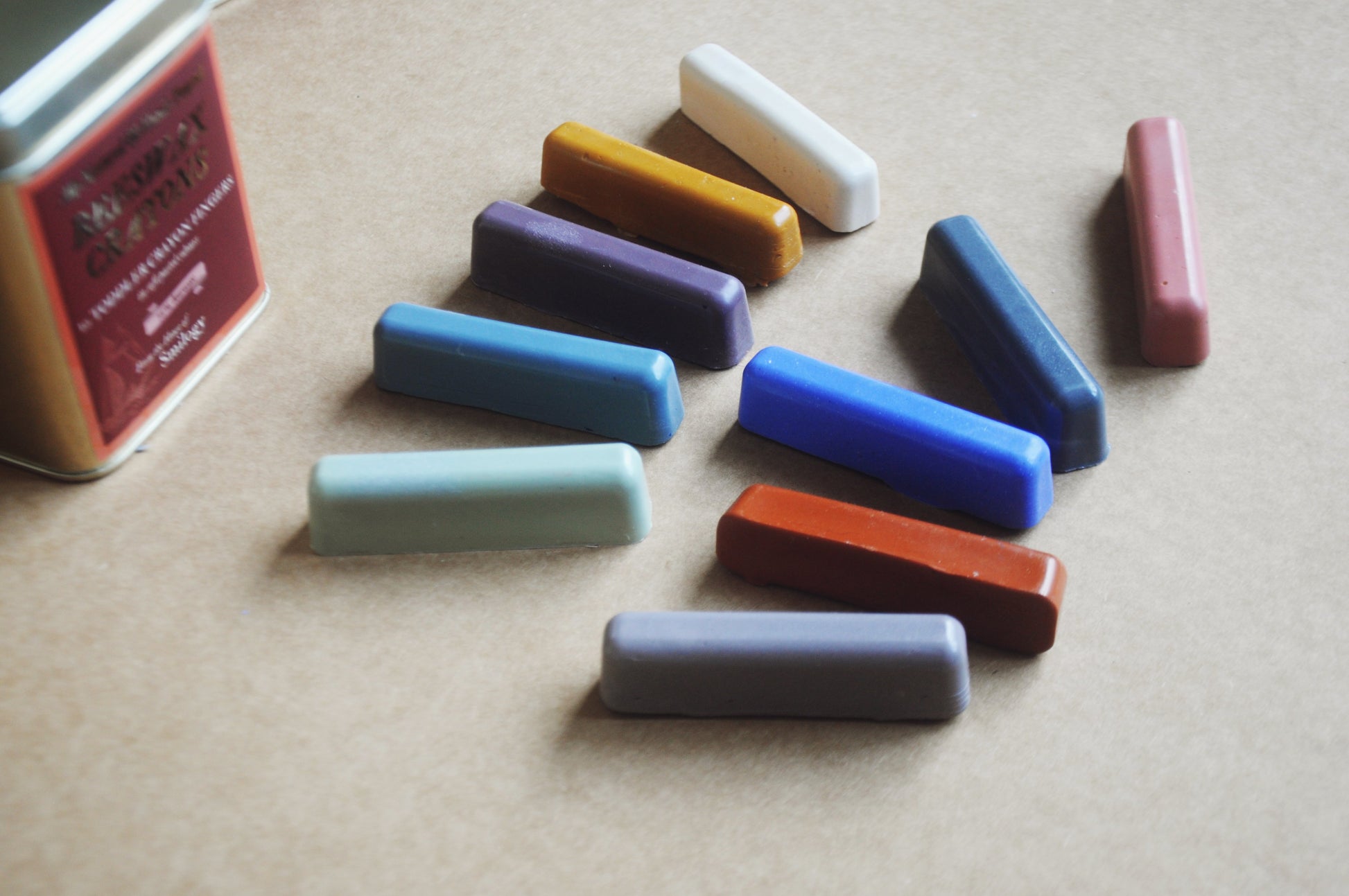 Set of colourful wax crayons in soft pastel shades with a tin container on a beige surface close up